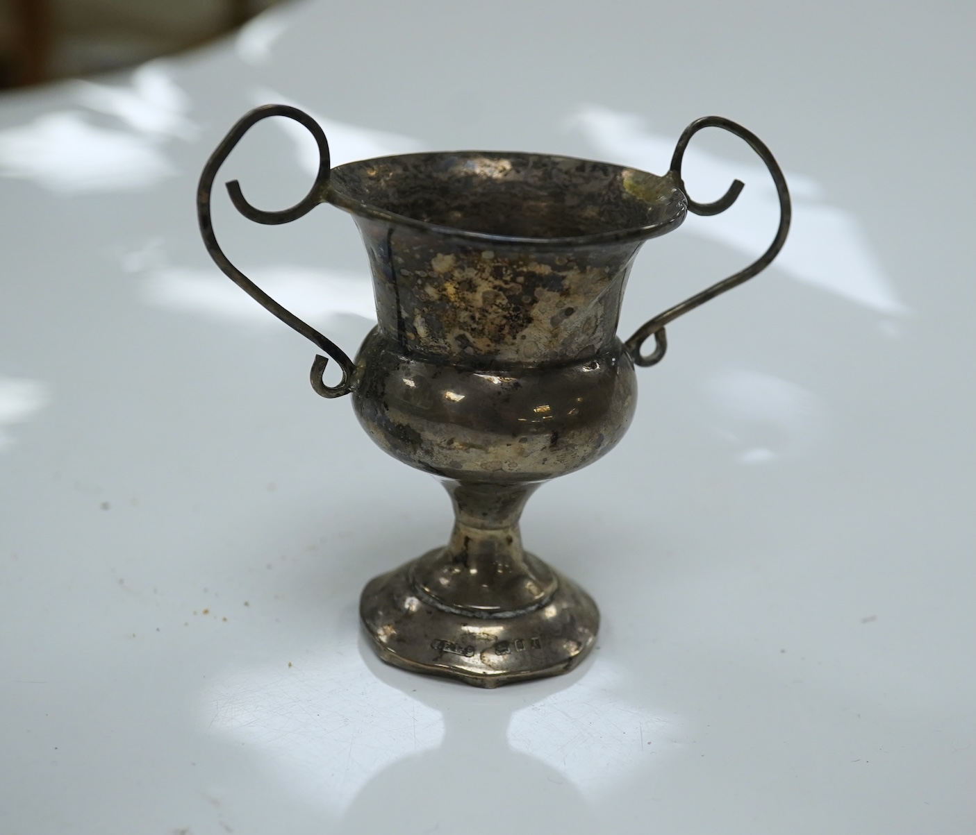 A William IV silver christening mug, London 1834, 10cm, a George III silver cream jug, London, 1799 and three small silver trophy cups. Condition - poor to fair